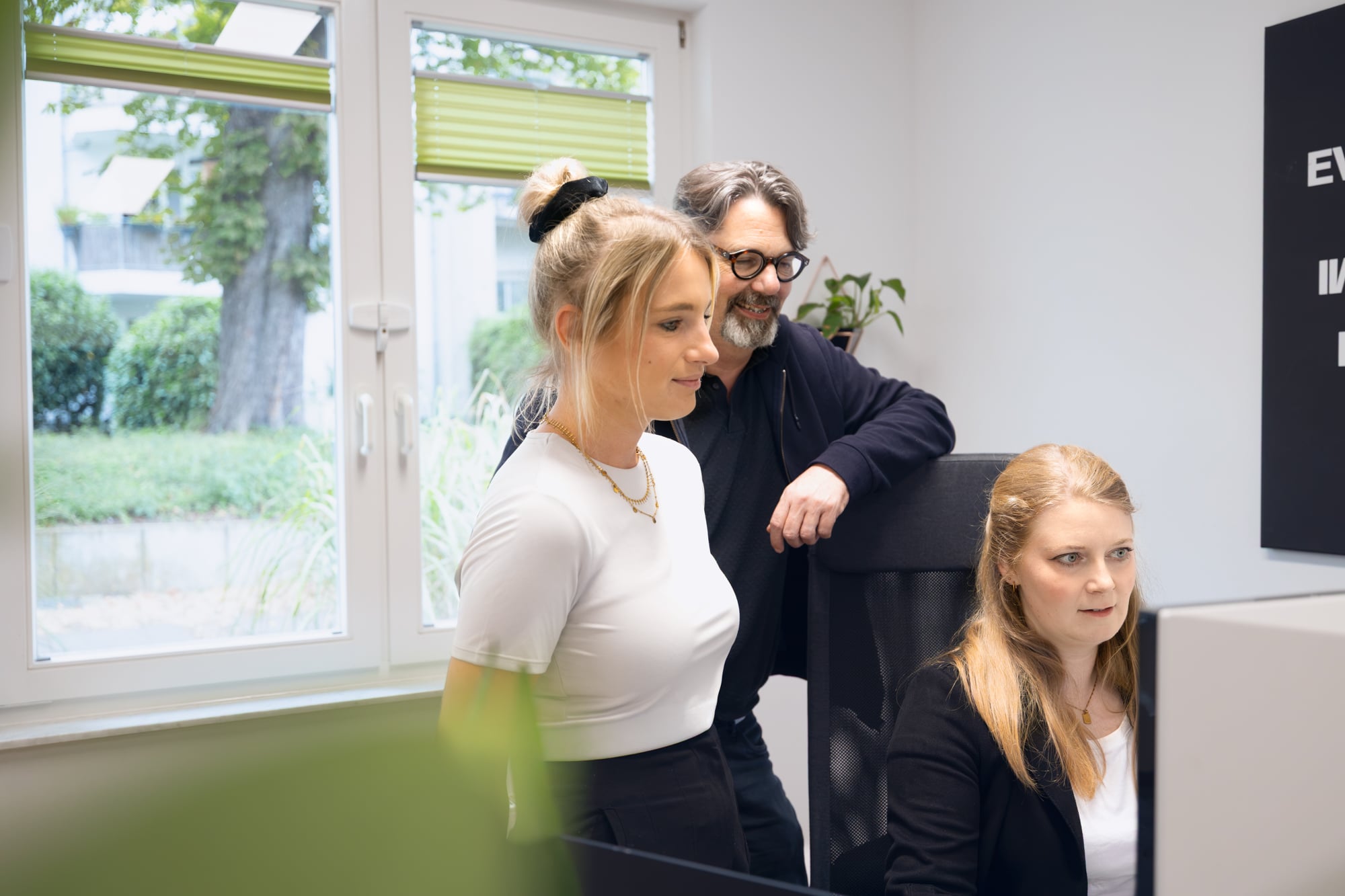 Drei Kolleg:innen schauen gemeinsam auf einen Bildschirm im Büro